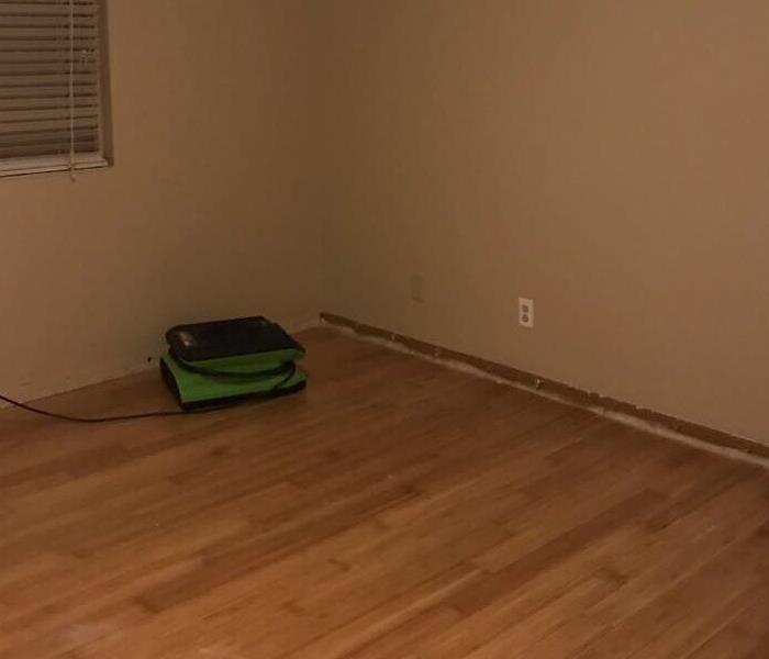 Wood floor with a green air mover working to remove the water damage. 