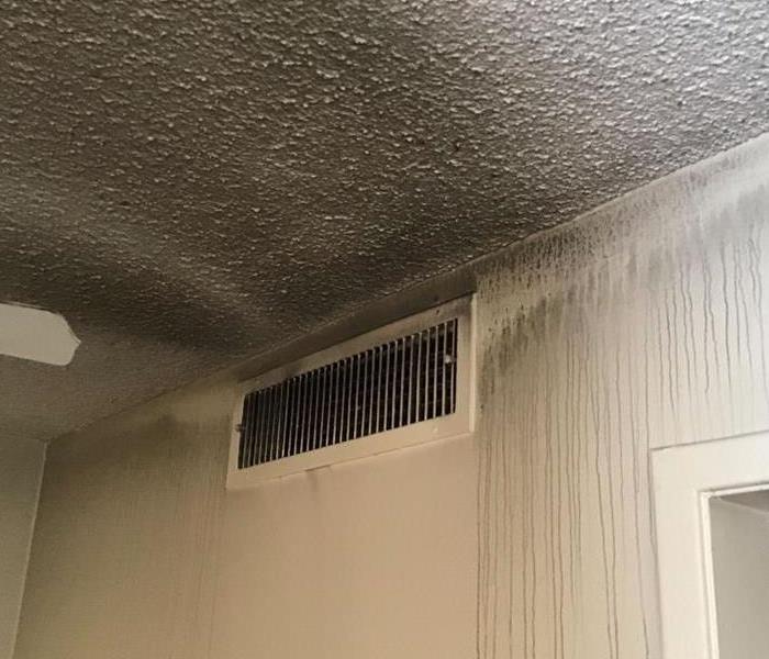 Wall with air vent covered in grey soot. 