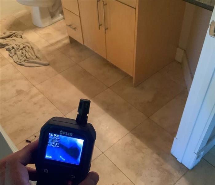 Moisture meter reading in a bathroom with a white toilet. 