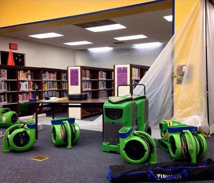 Five air movers and a dehumidifier placed in a library, drying up damaged area after water damage.